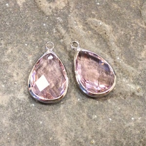 May include: Two teardrop-shaped pendants with a silver setting and a light pink crystal.