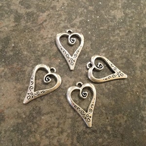 May include: Four silver heart-shaped charms with intricate designs. Each charm has a smaller heart inside the larger heart.