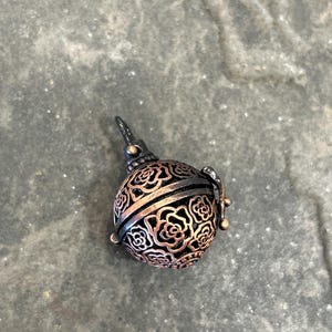 Peut inclure: Un petit charme rond en métal de couleur cuivre avec un motif délicat de roses. Le charme a une boucle en haut pour l'attacher à un collier ou un bracelet.