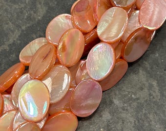May include: A strand of oval-shaped iridescent shell beads in shades of peach and pink.