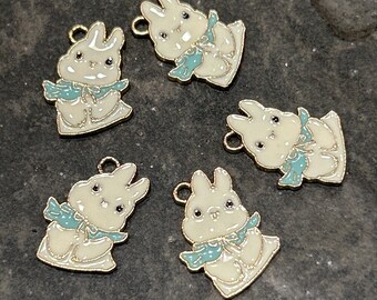 May include: Five gold-tone metal charms shaped like white bunnies with blue bows. The charms have a shiny finish and are perfect for adding a touch of whimsy to jewelry or crafts.