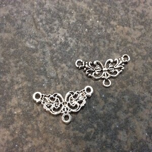 May include: Two silver filigree metal connector pieces with a decorative floral design. Each piece has three loops for attaching to other jewelry components.