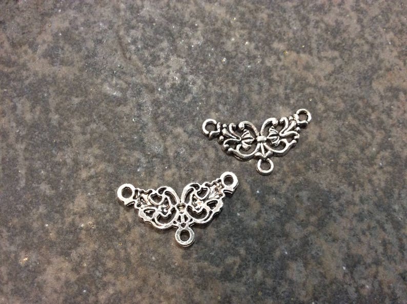 May include: Two silver filigree metal connector pieces with a decorative floral design. Each piece has three loops for attaching to other jewelry components.