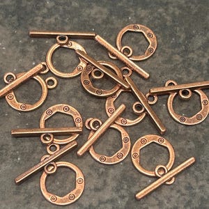 May include: A collection of copper-toned metal toggle clasps for jewelry making. Each clasp consists of a circular ring with a hexagonal inner cutout and a matching straight bar. The rings feature small circular indentations along the outer edge.