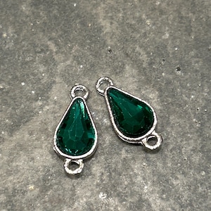 May include: Two silver teardrop-shaped charms with green crystal accents. The charms have a loop on each end for attaching to jewelry.