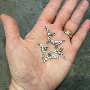 May include: Five silver-toned metal connector charms with a floral design. Each charm has three loops for attaching to jewelry or other crafts.