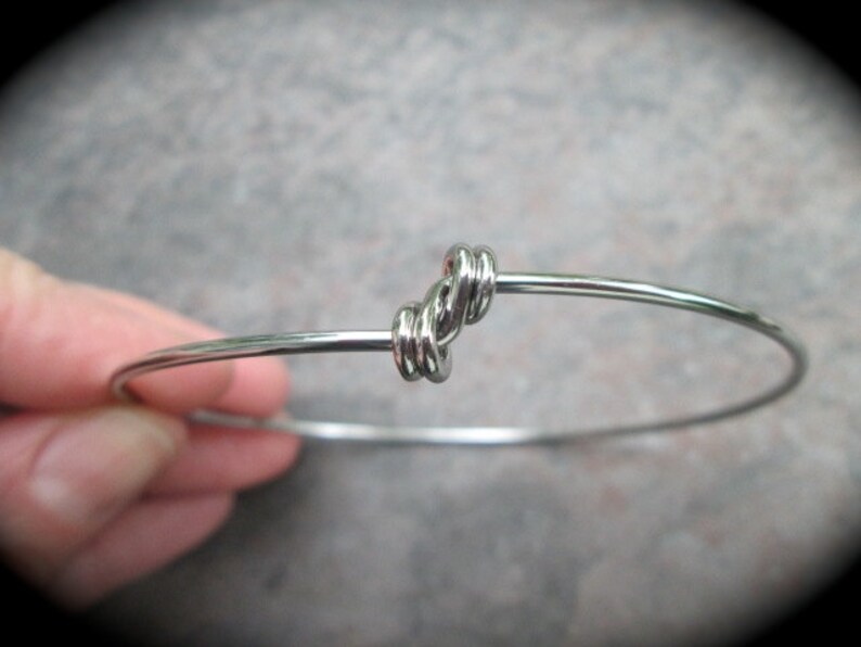 K&ouml;nnte beinhalten: Ein silbernes Armkettchen mit einem Knotendesign.