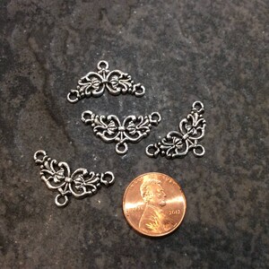 May include: Four silver-toned metal decorative embellishments with a floral design. Each embellishment has three points and a loop at the top.