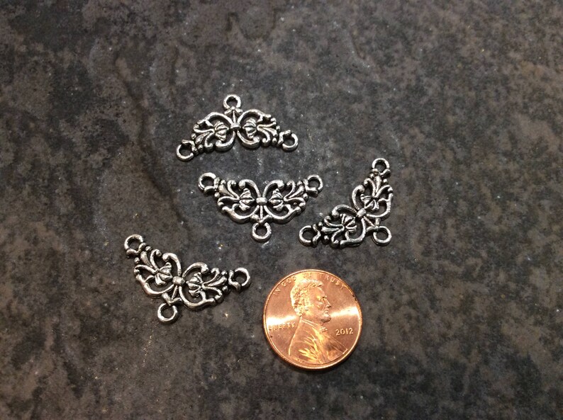 May include: Four silver-toned metal decorative embellishments with a floral design. Each embellishment has three points and a loop at the top.