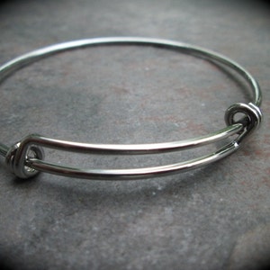May include: A silver expandable bangle bracelet with a simple design. The bracelet is made of metal and has a smooth finish.