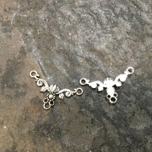May include: Two silver metal connector pieces with a floral design. The pieces have three loops for attaching to jewelry.