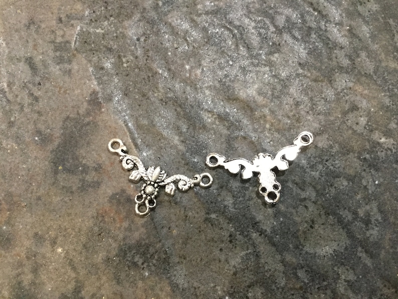 May include: Two silver metal connector pieces with a floral design. The pieces have three loops for attaching to jewelry.