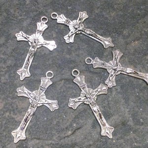 May include: A set of four silver-toned metal crucifix pendants, each featuring a detailed figure of Jesus on the cross with the letters INRI inscribed on a small plaque above the head and a circular halo design behind the figure.