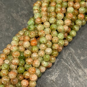 May include: A strand of green and orange agate beads with a crackled, textured surface. The beads are round and have a translucent appearance.