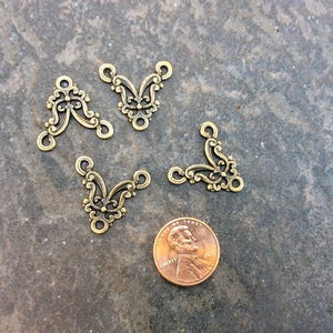 May include: Four gold-tone metal corner connectors with a decorative floral design. The connectors are approximately the size of a US penny.