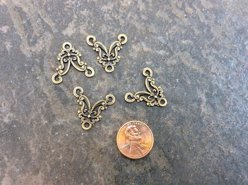 May include: Four gold-tone metal corner connectors with a decorative floral design. The connectors are approximately the size of a US penny.