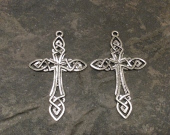 May include: Two silver Celtic cross charms with intricate knotwork designs. The crosses are detailed and have a slightly aged finish.