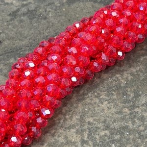 May include: Close-up of a strand of faceted red beads. The beads are a vibrant, translucent red, catching the light and reflecting multiple facets. The beads are strung together, forming a continuous line.
