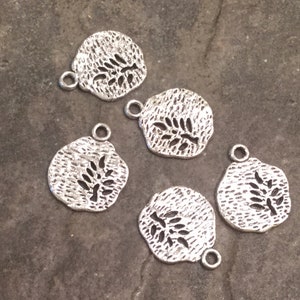 May include: Five silver metal charms with a textured surface and a cut-out design of a branch with leaves.