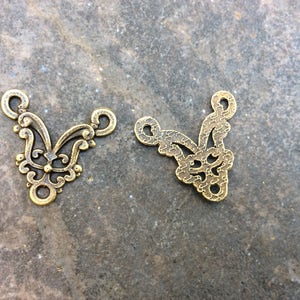 May include: Two gold-colored metal decorative pieces with intricate floral designs. The pieces are shaped like a V and have a hole at the top for hanging.