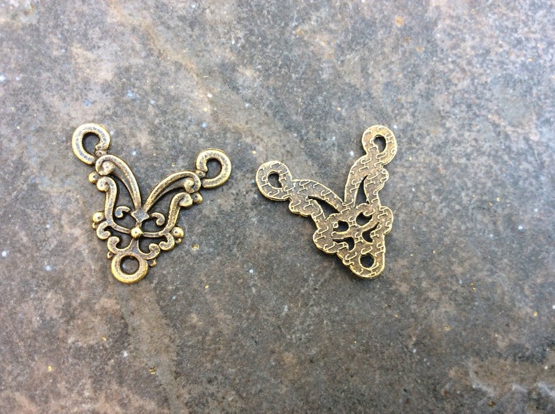 May include: Two gold-colored metal decorative pieces with intricate floral designs. The pieces are shaped like a V and have a hole at the top for hanging.