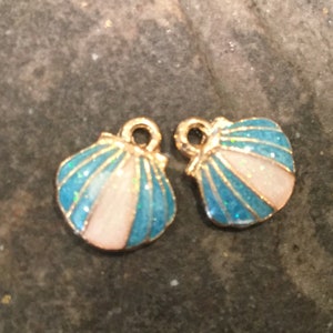 May include: Two gold-tone metal charms shaped like seashells. The shells are blue with white accents and have a glittery finish.