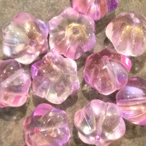 May include: A collection of ten pink and purple glass beads with a starburst shape and gold flecks. The beads are translucent and have a slightly iridescent finish.