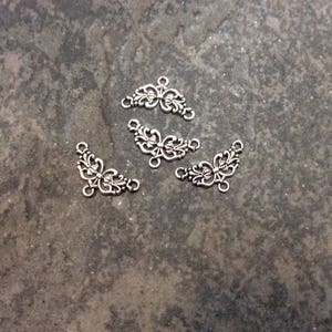 May include: Four silver-toned metal decorative embellishments with a floral design. Each embellishment has a curved shape and features intricate details.