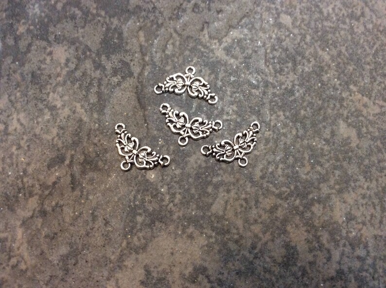 May include: Four silver-toned metal decorative embellishments with a floral design. Each embellishment has a curved shape and features intricate details.