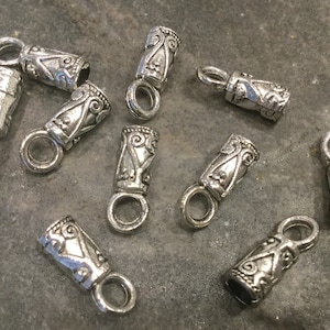 May include: Ten silver-toned metal end caps with a decorative design. Each end cap has a small loop for attaching to a cord or chain.