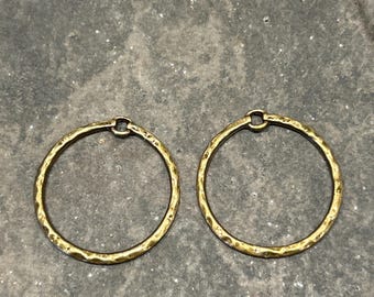 May include: Two gold-toned hammered metal hoop earrings. The hoops are smooth and have a slightly textured finish.