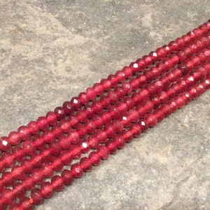 May include: A strand of red faceted gemstone beads. The beads are small and have a smooth, polished finish.