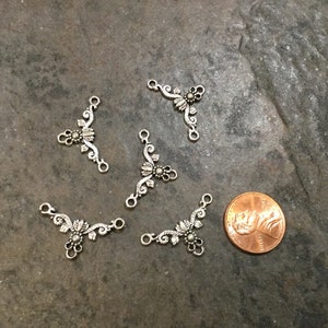 May include: Five silver-toned metal connector charms with a floral design. Each charm has three loops for attaching to jewelry or other crafts.