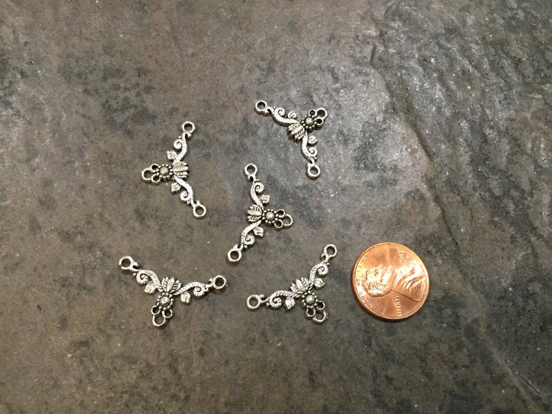 May include: Five silver-toned metal connector charms with a floral design. Each charm has three loops for attaching to jewelry or other crafts.