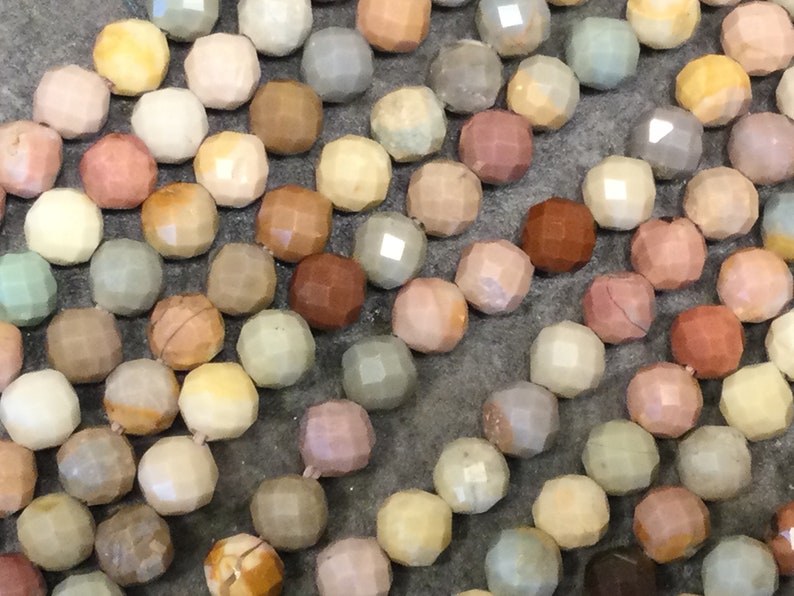 May include: A strand of colorful faceted gemstone beads. The beads are various shades of brown, pink, green, and yellow. The beads are all round and have a faceted finish.