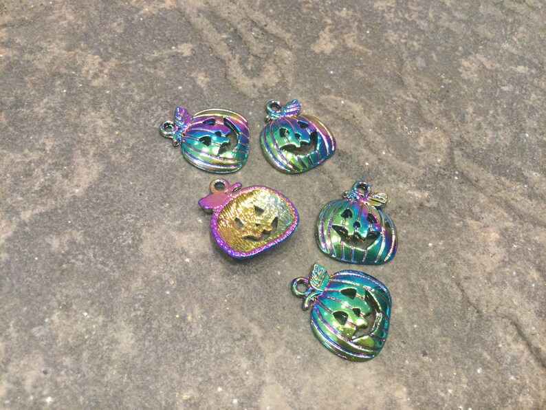Pu&ograve; includere: Cinque ciondoli a forma di zucca in metallo iridescente con facce di jack-o'-lantern. I ciondoli sono un mix di verde, blu e viola.