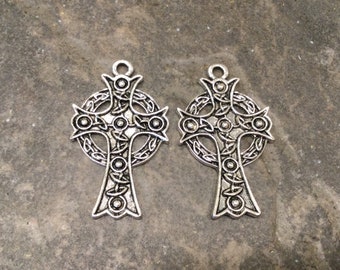 May include: Two silver Celtic cross charms with intricate knotwork designs. The crosses have a circular halo around them and are detailed with small beads.
