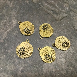 May include: Five gold-toned metal charms with a leaf design. Each charm has a loop for attaching to a necklace or bracelet.