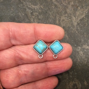 May include: Two turquoise blue square-shaped earrings with silver-toned metal settings and a loop at the bottom.