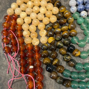 May include: A rainbow of gemstone beads, including carnelian, citrine, tiger's eye, aventurine, and sodalite. The beads are strung on pink thread and are ready to be made into jewelry.