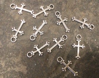 May include: Ten silver-toned metal cross charms with a decorative design. The charms have a loop at the top for attaching to jewelry or other crafts.