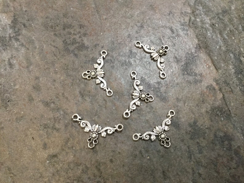 May include: Six silver-toned metal connector charms with a floral design. Each charm has three loops for attaching to jewelry or other crafts.