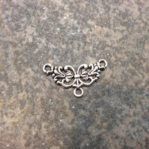 May include: Silver-toned metal connector with a decorative butterfly design. The connector has two loops on the sides and a single loop on the bottom.