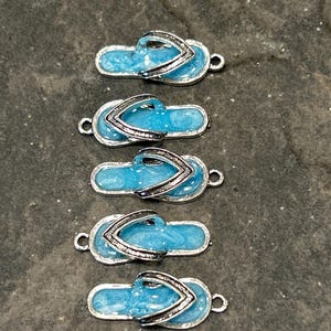 May include: Five blue flip flop charms with silver accents. The charms have a sparkly finish and are perfect for adding a summery touch to jewelry or crafts.