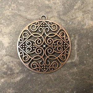 May include: A round, copper-colored pendant with a decorative, intricate design of swirls and dots.