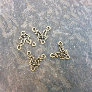 May include: Four gold-toned metal connector pieces with a decorative, ornate design. Each piece has three loops for attaching jewelry or other crafts.