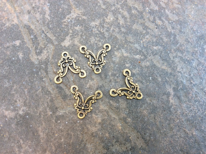 May include: Four gold-toned metal connector pieces with a decorative, ornate design. Each piece has three loops for attaching jewelry or other crafts.