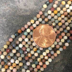 May include: A strand of multi-colored gemstone beads, each bead is faceted and has a unique pattern. The beads are approximately the size of a US penny.