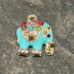 May include: A turquoise elephant charm with gold accents and colorful rhinestones. The elephant has a gold trunk, ears, and feet, and a loop at the top for attaching to a necklace or bracelet. The charm is a cute and colorful accessory.