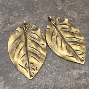 May include: Two antique gold leaf charms with a detailed textured design. The leaves have a small loop at the top for attaching to jewelry or other crafts.